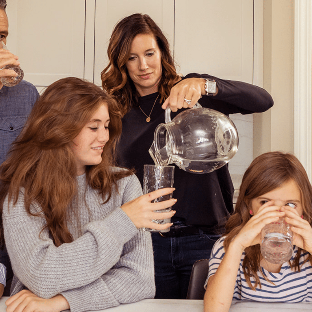 Mom pouring water from pitcher into daughter's cup.